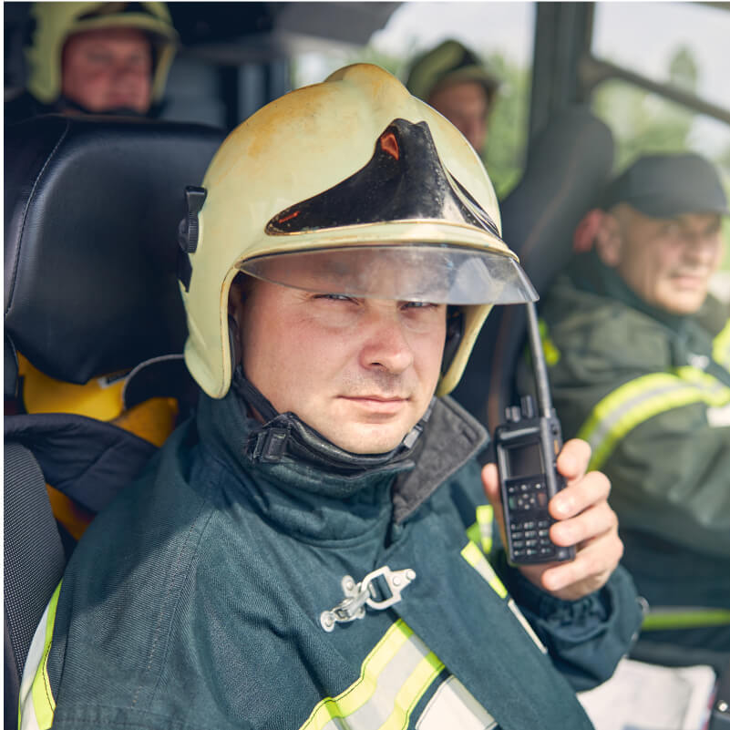 A man wearing a fireman's helmet is holding a cell phone, appearing focused and ready for communication.