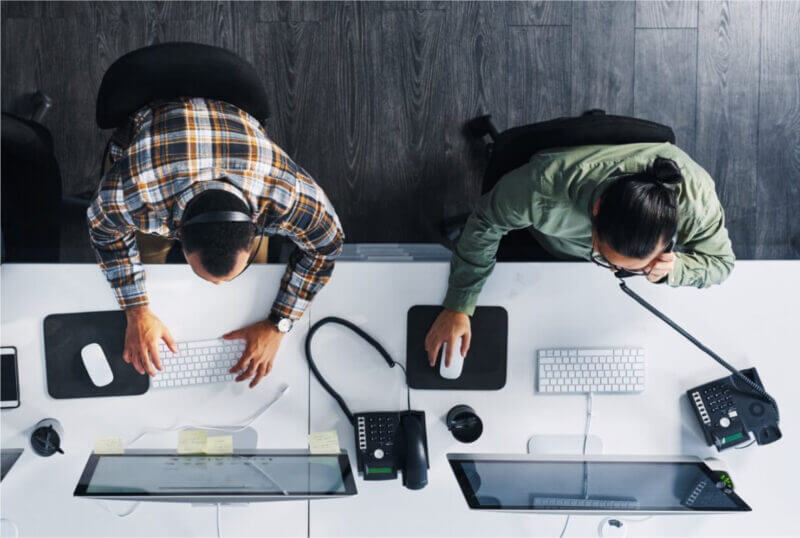 Two individuals collaborating at a desk, focused on their computers, engaged in a productive work environment.