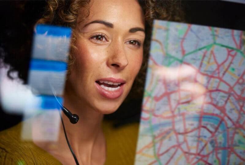 A dispatcher woman wearing a headset, intently studying a map for navigation and coordination purposes.