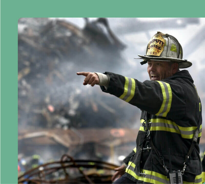 A fire chief in uniform points upward, indicating something significant in the sky with a focused expression.