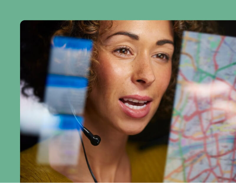 A dispatcher woman wearing a headset, intently studying a map for navigation and coordination purposes.