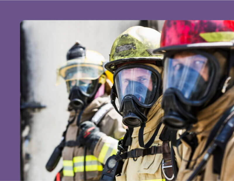 Three first responders in gas masks prepare for action, showcasing their commitment to safety and emergency response.